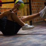 A man and woman perform core exercises with a medicine ball in a brick wall gym.